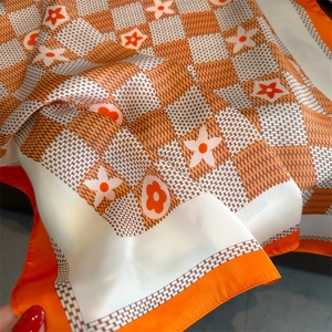 Detail of orange floral checkerboard silk scarf showing satin texture and vibrant print