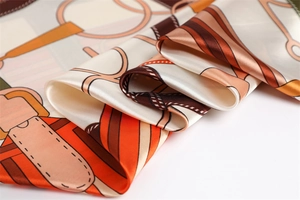 Detail of silk-like satin scarf with equestrian chain print in orange and brown