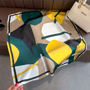 Detail of a geometric color-block silk scarf styled on a leather sofa with accessories