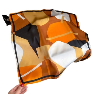 Abstract geometric silk scarf in orange and brown tones held by hand on white background