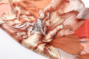 Close-up of silk scarf featuring vibrant orange floral patterns and satin texture