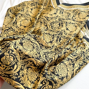 Detail of silk scarf showing black and gold baroque floral print with Greek key border