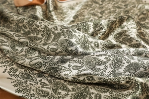 Detail of silk-like satin fabric showing green paisley pattern and soft smooth texture
