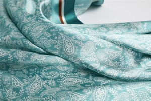 Detailed macro view of smooth paisley satin scarf with elegant teal and white patterns