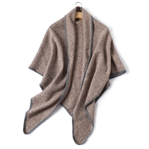 Detail view of khaki knit cashmere-like shawl with grey stitched edges on a wooden hanger
