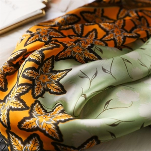 Orange and green maple leaf print silk scarf displayed in elegant draped layers