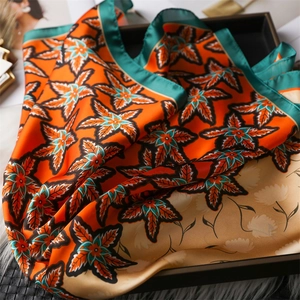 Macro detail of silk scarf featuring orange maple leaf print and green hem on wood tray