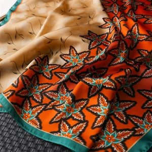 Detail of silk scarf showing orange maple leaf print and smooth glossy texture fabric