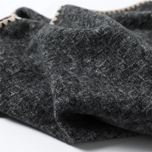 Macro detail of dark grey cashmere-like knit fabric with beige crochet stitched edges