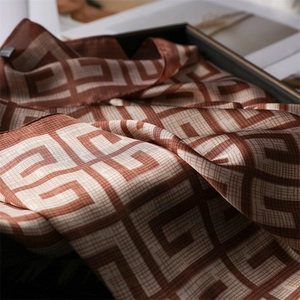 Détail d'un carré de soie de luxe avec motif monogramme géométrique marron sur coffret