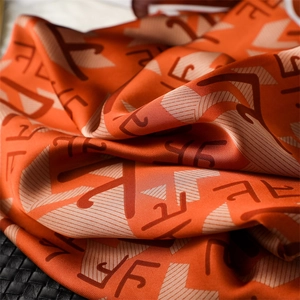 Détail macro d'un foulard en satin orange avec motif géométrique marron et fini soyeux