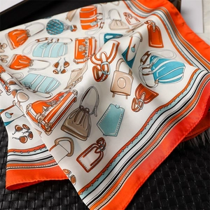 Detailed view of luxury silk scarf showing vintage handbag prints and orange hem border