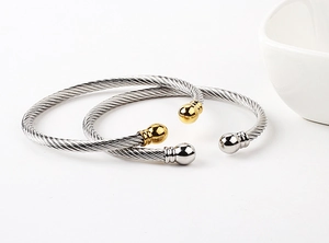 Detail of twisted cable cuff bracelets in 18k gold plating with metallic bead ends