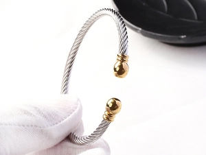 Detail of twisted cable steel bangle with silver texture and golden bead caps