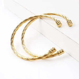 Detail of twisted cable gold bangles set with layered cylinder end caps on a white podium