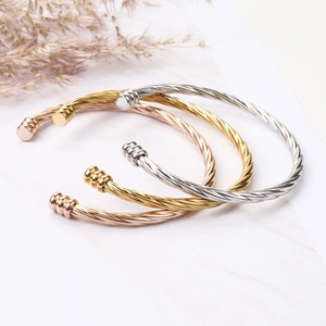 Detail of twisted cable bangles in gold, silver and rose gold on white marble surface