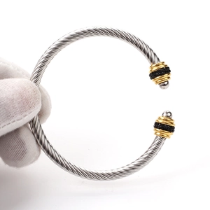 Macro detail of twisted cable steel bangle featuring black stones and gold-toned accents