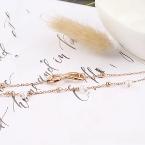 Gros plan d'une chevillère rose dorée avec symbole infini, perles blanches et chaînes