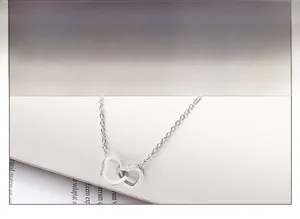 Vue détaillée du pendentif double cœur entrelacé sur une fine chaîne argentée
