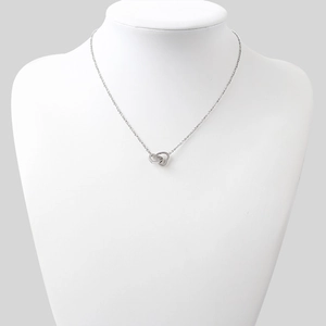 Détail du collier avec deux cœurs entrelacés présenté sur un buste d'exposition blanc