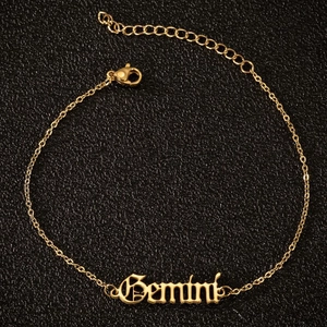 Makroaufnahme goldene Sternzeichen-Fußkette Zwillinge in altenglischer Schrift auf Leder