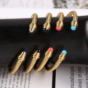 Close-up of four twisted 18K gold-plated steel bangles with colorful gemstone end caps