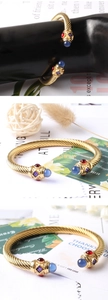 Dettaglio del bracciale rigido dorato a treccia con pietre colorate e confezione regalo