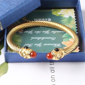 Dettaglio del bracciale a cavo dorato con pietre rosse e nere su portagioie blu