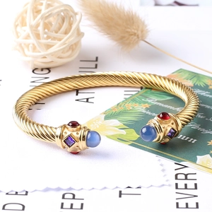 Dettaglio del bracciale a cavo dorato intrecciato con pietre preziose blu e rosse
