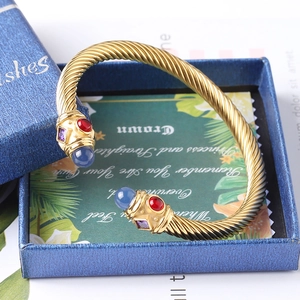 Dettaglio macro del bracciale rigido a treccia dorata con gemme colorate alle estremità