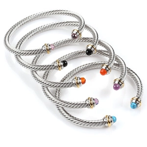 Macro detail of five twisted cable cuff bracelets with colorful gemstones and 18K gold trim