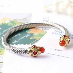 Dettaglio ravvicinato di un bracciale a cavo d'argento con punte dorate e gemme rosse