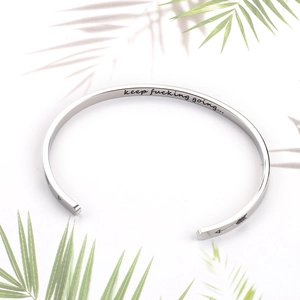 Macro detail of silver stainless steel cuff with keep fucking going engraved message