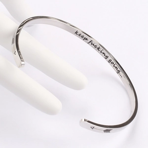 Macro view of silver stainless steel cuff bracelet with motivational engraving and arrow symbol