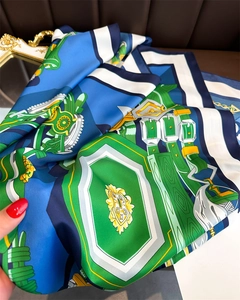 Detailed view of silk scarf fabric showing retro chain patterns and vibrant blue green colors