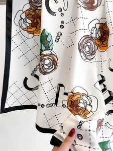 Detailed close-up of camellia pattern silk scarf with smooth draped texture and black border