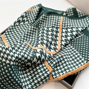 Dettaglio foulard in seta pied-de-poule verde scuro con bordo arancio e scritte fashion