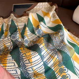 Macro shot of silk-like scarf featuring geometric triangle patterns and monogrammed border