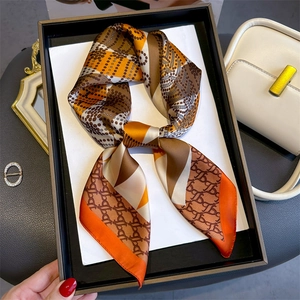 Close-up of geometric monogram silk scarf with orange and coffee tones in a luxury gift box