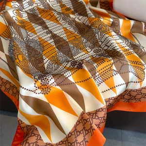 Detail of silk-like satin scarf featuring orange rhombus patterns and luxury TB monogram print