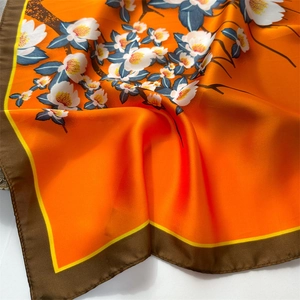 Close-up of orange silk scarf with elegant floral prints and smooth satin texture