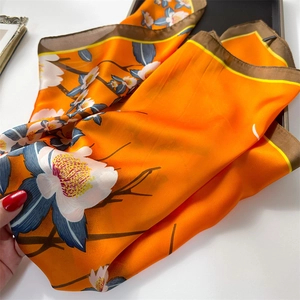 Detail of vibrant orange floral silk scarf showing satin texture and floral patterns