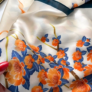 Close-up of silk scarf fabric showing cream base with orange flowers and navy blue hem