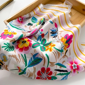 Detailed close-up of vibrant floral print on white silk-like square scarf