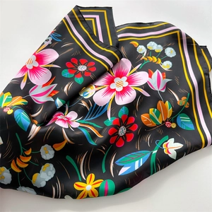 Detail of floral print silk scarf featuring pink flowers and striped border on black fabric