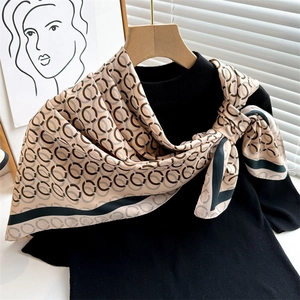 Beige chain print square silk scarf tied as a bow on a black top for women