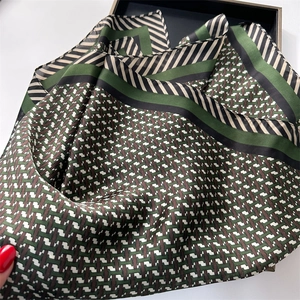 Détail d'un foulard en soie à motif géométrique H en vert et noir dans son coffret luxe