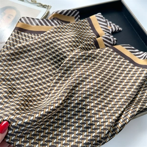 Détail d'un foulard carré en soie avec motif géométrique et bords en sergé dorés et marron