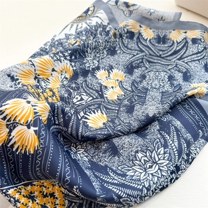 Close-up of silk-like scarf featuring yellow sunflowers and palm leaves on deep blue twill