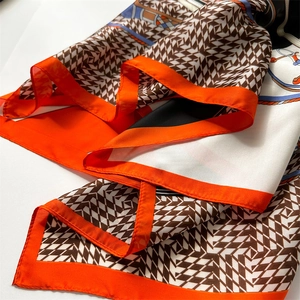 Macro detail of silk scarf featuring geometric H patterns and elegant orange borders